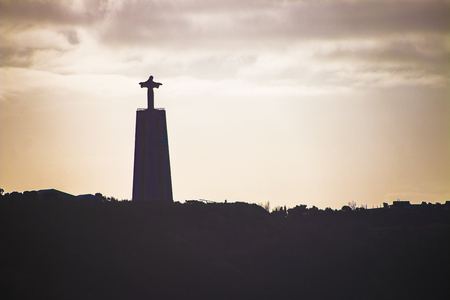 Silhouette of a statue of Christ in the background of the setting sun in Lisbon, Portugalの写真素材
