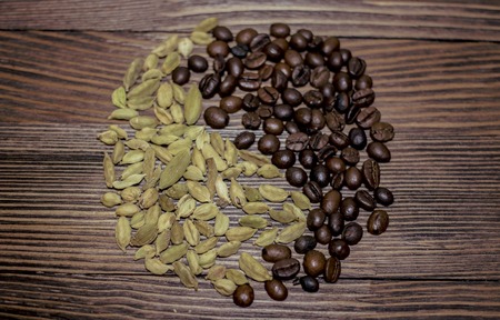 Whole grains of coffee and cardamom together on a table.の写真素材