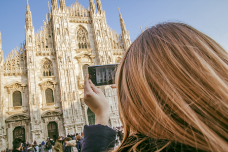A girl with blond hair takes pictures of the Duomo in Milan with a mobile phone.の写真素材