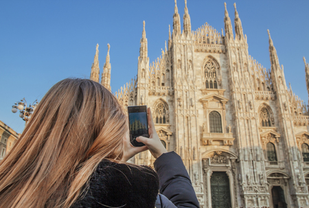 A girl with blond hair takes pictures of the Duomo in Milan with a mobile phone.の写真素材