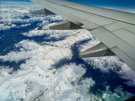 Mountains and white snow on the tops under the wing of the aircraft during the flight.の写真素材