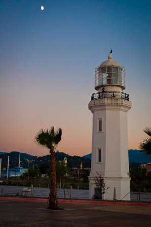 Lighthouse on the beach, against the backdrop of mountains. Architectural photography at dusk. Stone lighthouse in the form of an octagonal tower built in 1882, illuminated by red lights at night.の写真素材