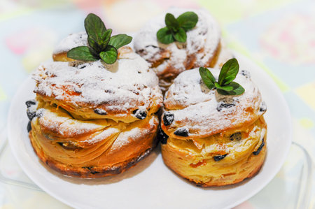 Easter muffins, craffin in white sugar powder, raisins and mint leaves, on a white plate.