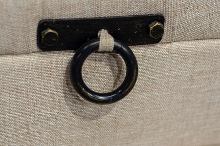 Retro furniture fittings for upholstered pouffe and banquet, metal black ring on fabric background, upholstered furniture with decorative handleの写真素材