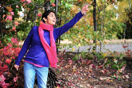 Indian beautiful girl holding orange maple leaf in autumn park