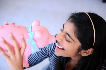 Cheerful Indian girl kissing her piggybankの写真素材