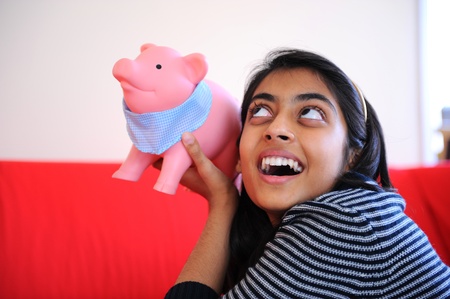 Excited Indian girl listening he soud of coins from piggybankの写真素材