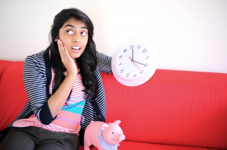 girl sitting with piggybank and holding clock is in stressの写真素材