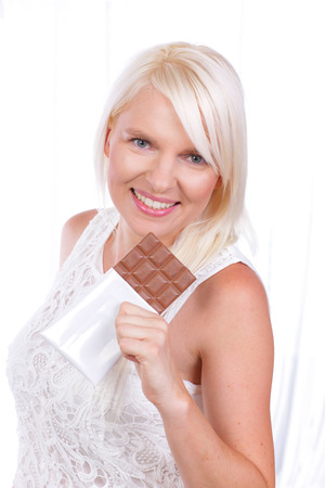 Young blond woman holding a bar of chocolateの写真素材