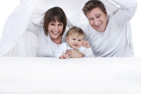 Happy family with toddler under white sheetsの写真素材