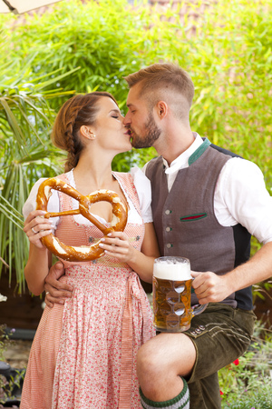 Bavarian couple in traditional costume with beer and brezel outdoor in a beergardenの写真素材