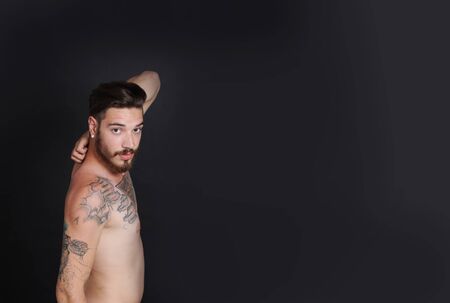 Young urban man with tattoos stripped to the waist in front of black backgroundの写真素材