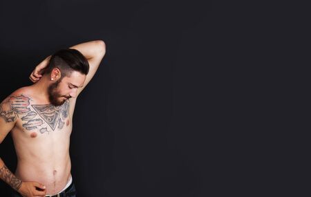 Young urban man with tattoos stripped to the waist in front of black backgroundの写真素材