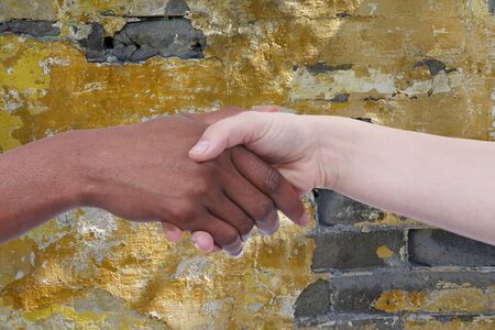 Handshake of african und european woman in front of a stone wallの写真素材