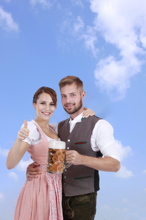 Happy young couple with beer and traditional costume in front of blue skyの写真素材