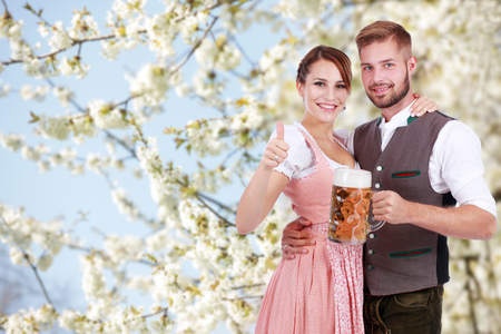 Happy young couple with beer and traditional costume in front of a flowering treeの写真素材