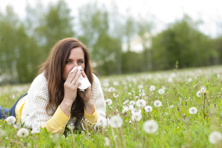 Unhappy middle age woman with hay fever and handkerchief lying in the grassの写真素材