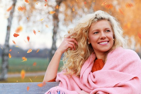 Matured woman enjoys leisure time in autumn outdoor sitting on a benchの写真素材