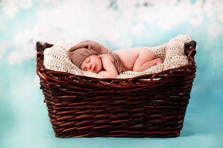 newborn baby with cute hat lying in a fur basketの写真素材