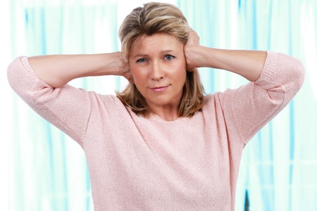 mature woman blocks her ears from noise and painの写真素材