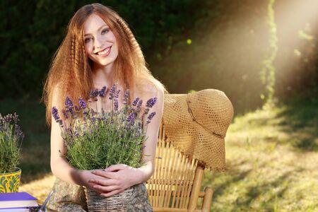 Attractive red haired woman with straw hat in summer garden with lavenderの写真素材