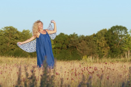 Happy mature woman is playing with a big shawl  in nature in summerの写真素材