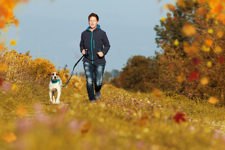 Sportive woman runs with her dog on a leash in autumn exterior shotの写真素材