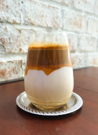 Dirty Coffee - A glass of espresso shot mixed with cold fresh milk put on wood table behide white brick wall in coffee shop cafe and restaurantの写真素材