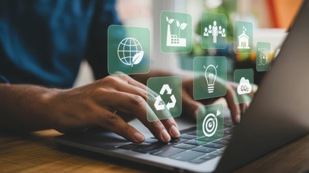 Hands typing on a laptop keyboard with floating green square icons displaying white symbols for environment and business concepts.の素材
