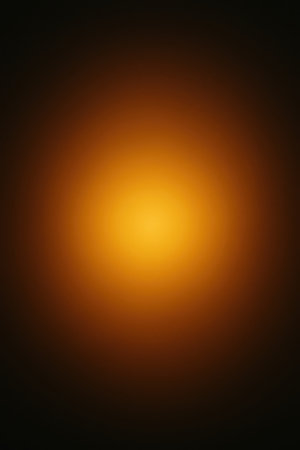 A soft radial gradient transitions from a bright yellow-orange glow at the center to dark brown and black at the edges. The central area is luminous and circular, with the color gradually darkening outwards, creating a smooth, atmospheric effect.の素材