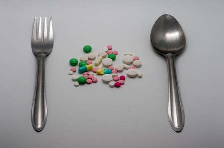 Multiple color drug and pills with folk and knife isolated on white background.の写真素材