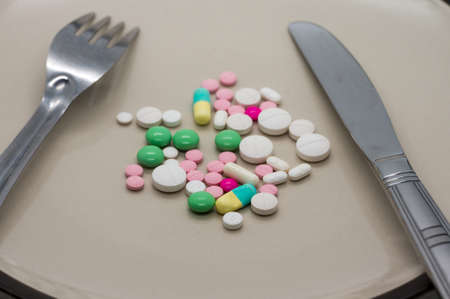 Multiple color drug and pills on ceramic dish with folk and knife.の写真素材