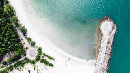 Aerial photo of breakwater the beach with view of group of people and small fishing boat on white sand beach, trees and clear sea water.の写真素材