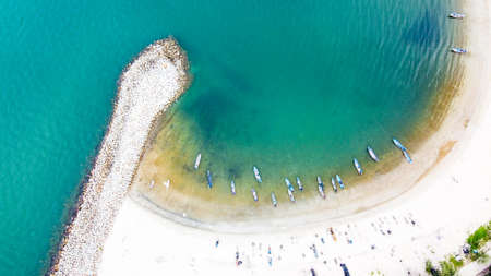 Aerial photo of breakwater the beach with view of group of people and small fishing boat on white sand beach, trees and clear sea water.の写真素材