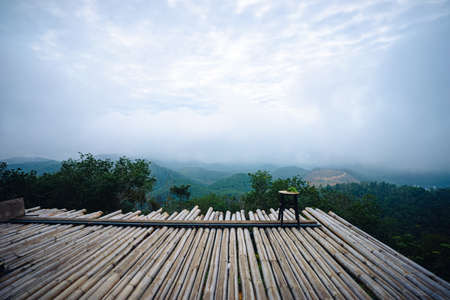 Wooden chair on bamboo platform in the middle of the forest with view of mountain, green trees and fog.の写真素材