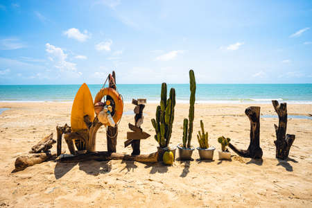 Cactus, wooden block, surf board on the beach with blue sea water, clear blue sky and small white...