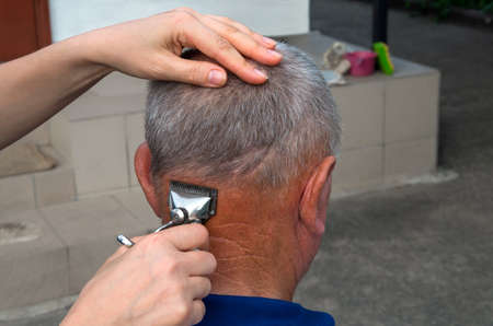 Improvised hairdresser's salon on a rural farm. Woman mows a man after harvest before bathing in the bath.の写真素材