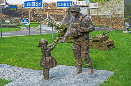 Dnipro, Ukraine - May 19, 2016: Open air museum dedicated to war in the Donbass. Little girl has treated apple Ukrainian soldierのeditorial素材