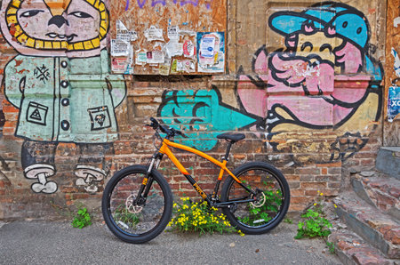 Dnipro, Ukraine - May 11, 2020: New orange and not locked mountain bike stands near the wall with graffitiのeditorial素材