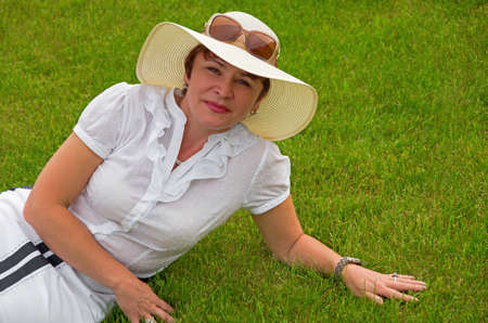 Close-up portrait of smiling female in hat on a green lawnの写真素材