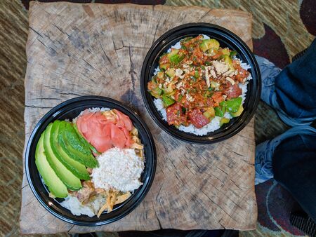 Two spicy tuna and salmon poke bowls with avocado, ginger, onions, and white rice, sitting on a wooden tableのeditorial素材