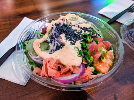Spicy ahi tuna and salmon poke bowl, filled with avocado, mixed greens, rice, and other fresh crisp...