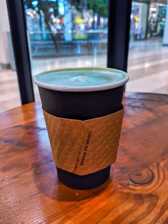 Piping hot matcha green tea latte with the lid off, sitting isolated on a wooden cafe table at a mallの写真素材