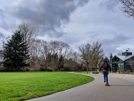 Woodinville, WA / USA - circa February 2020: Young adult skateboarding down a walking path on a popular day at the Wilmot Gateway Riverfront Park in Woodinville.のeditorial素材