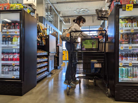 Kirkland, WA / USA - circa April 2020: Woman wearing a protective mask and gloves while checking out behind a plexiglass barrier at a checkout counter at QFC amidst the coronavirus pandemic.のeditorial素材