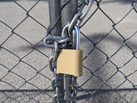 Close up of a yellow padlock and chain keeping a chainlink fence sealed