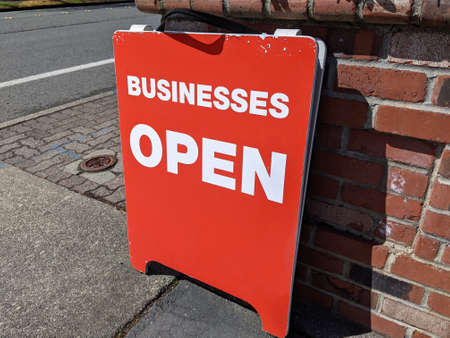 View of a bright red 'Businesses Open' sign on a street corner in a busy downtown areaの写真素材