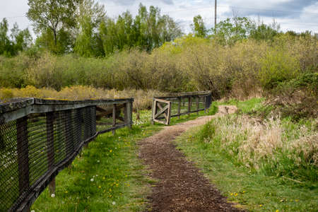 Beautiful view of a dirt path by a wooden fenced in farm on a cloud filled, sunny day