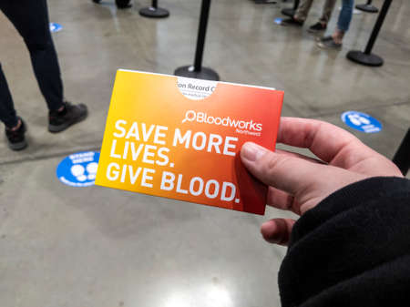 Seattle, WA USA - circa May 2021: View of a caucasian hand holding a Bloodworks Northwest card, containing their covid 19 coronavirus shot records.のeditorial素材