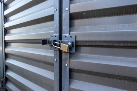 Angled view of a yellow padlock keeping two large metal doors locked up tight in an outdoor storage facilityの写真素材